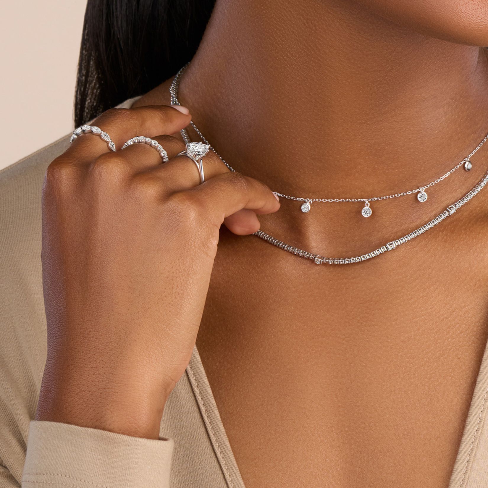 woman wearing an engagement ring with wedding rings on alternative fingers with stacked necklaces