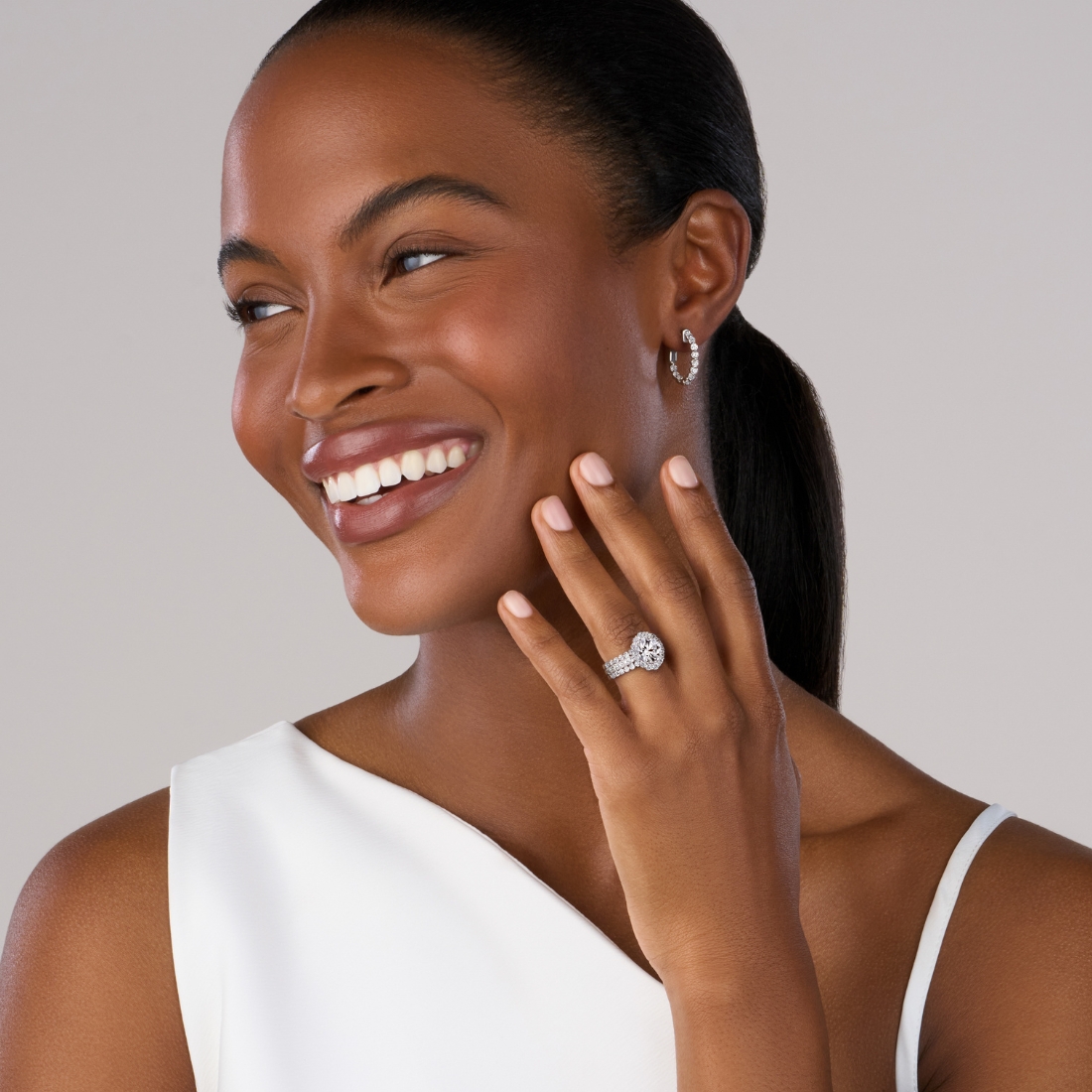 woman wearing a white asymmetrical top with a split shank halo engagement ring and hoop earrings